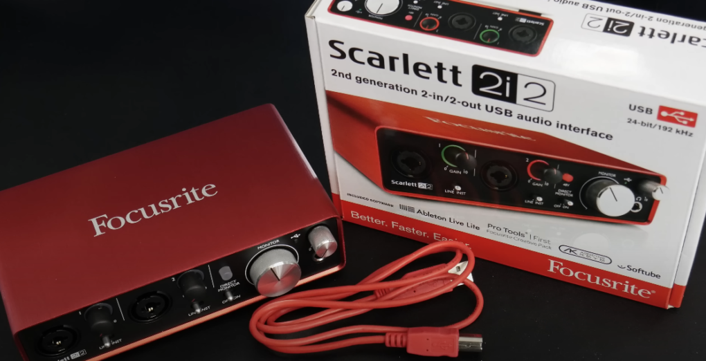 Photo of a red Focusrite Scarlett 2i2 audio interface on a table, with wire and box