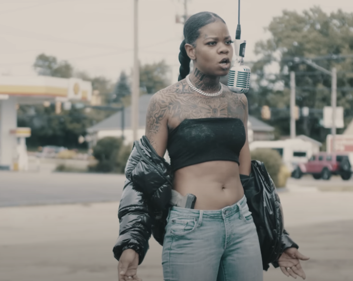 Photo of a woman wearing a tube top, with visible tattoos, standing outdoors and singing