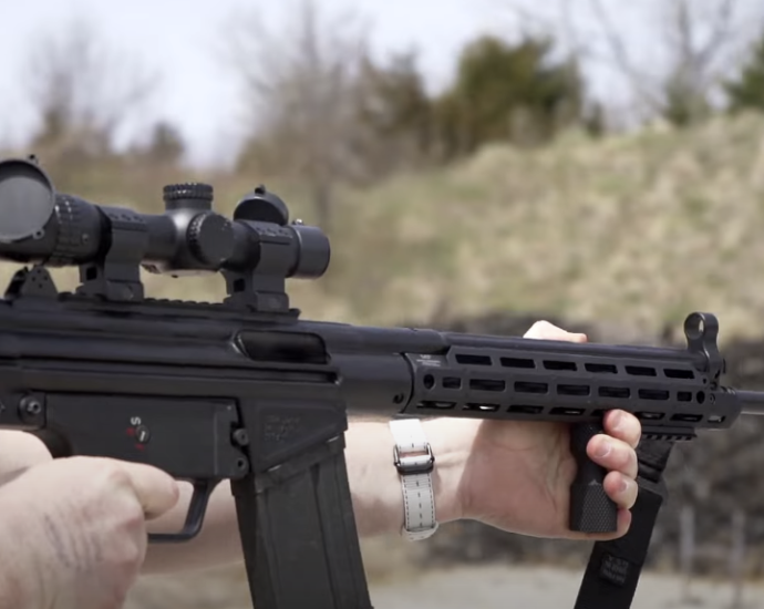 Photo of a guy wearing a hat, holding an automatic firearm