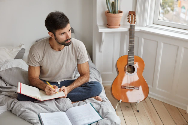 A person writing lyrics on a notepad, surrounded by musical instruments