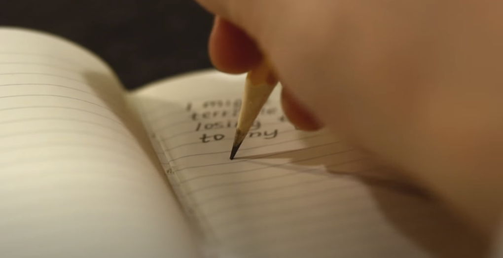 Photo of a notebook and a pencil, with something being written on the pages