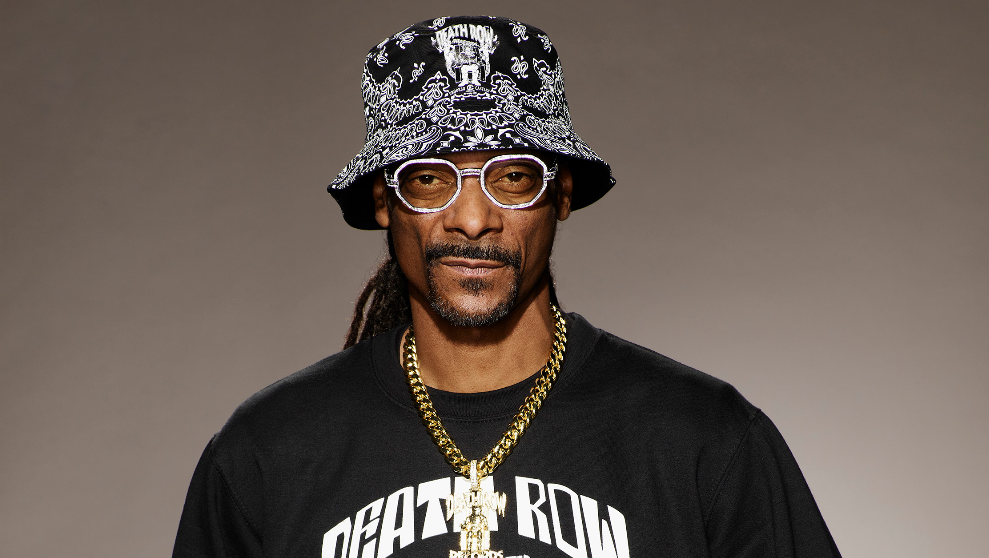 famous rap artist Snoop Dogg stands in a black cap and glasses on a brown background