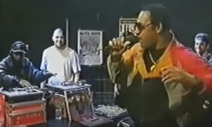 Photo of DJ Kool Herc holding a microphone while singing