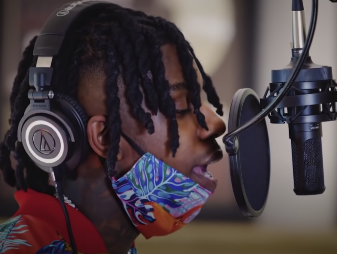 Photo of a man with dreadlocks singing into a recording microphone with a filter attached