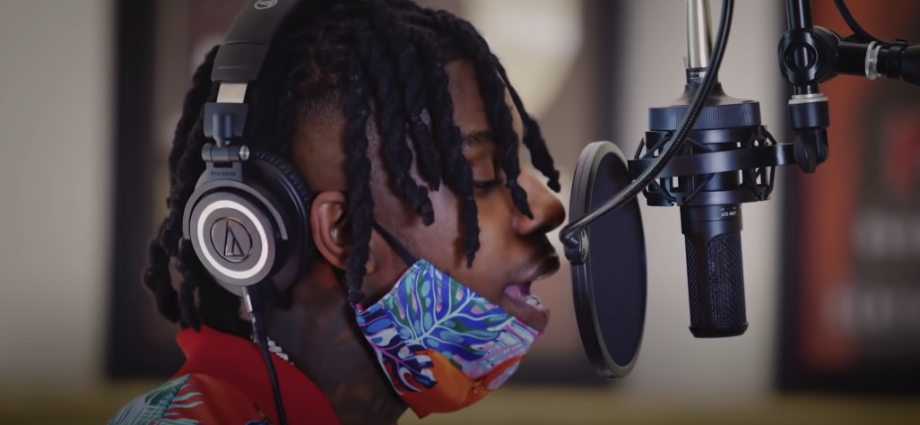 Photo of a man with dreadlocks singing into a recording microphone with a filter attached