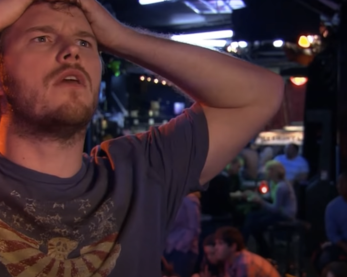 Photo of a man inside a bar, holding his head with both hands, appearing deep in thought