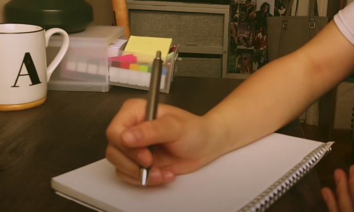 Photo of a hand holding a pen, poised to write something on a notebook