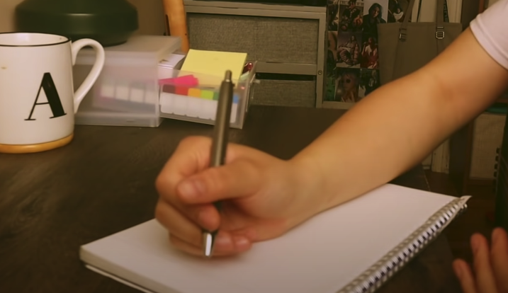 Photo of a hand holding a pen, poised to write something on a notebook