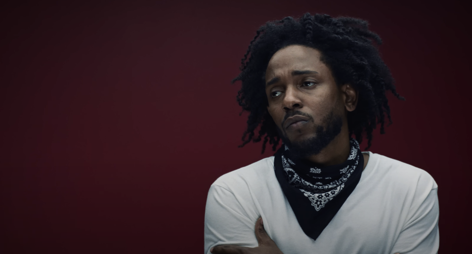 Photo of a guy with dreadlocked hair, wearing a white shirt, gazing into the distance against a red background