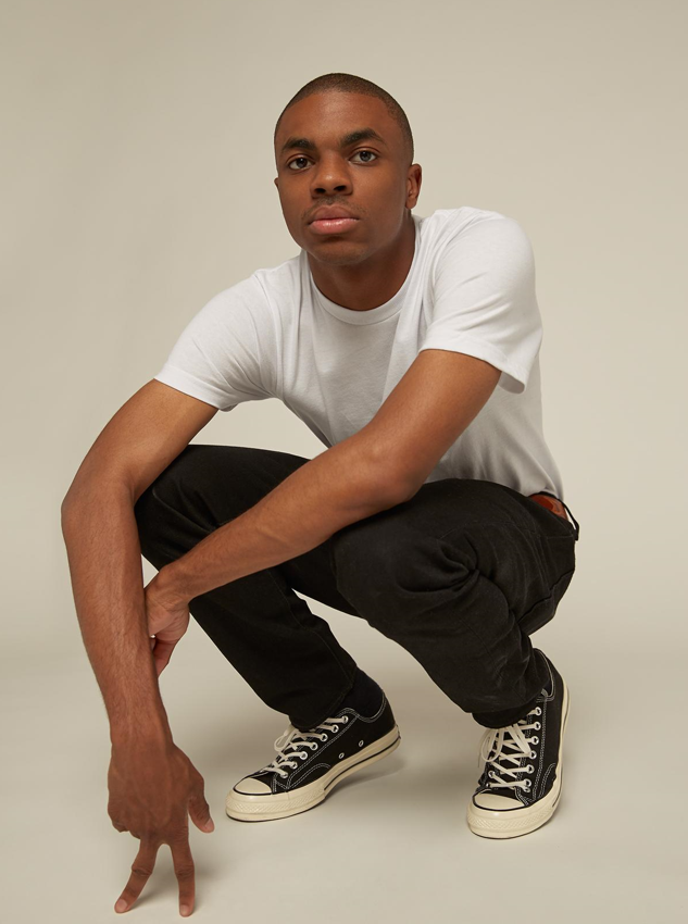 American rapper Vince Staples squatting in a white T-shirt, black jeans and sneakers