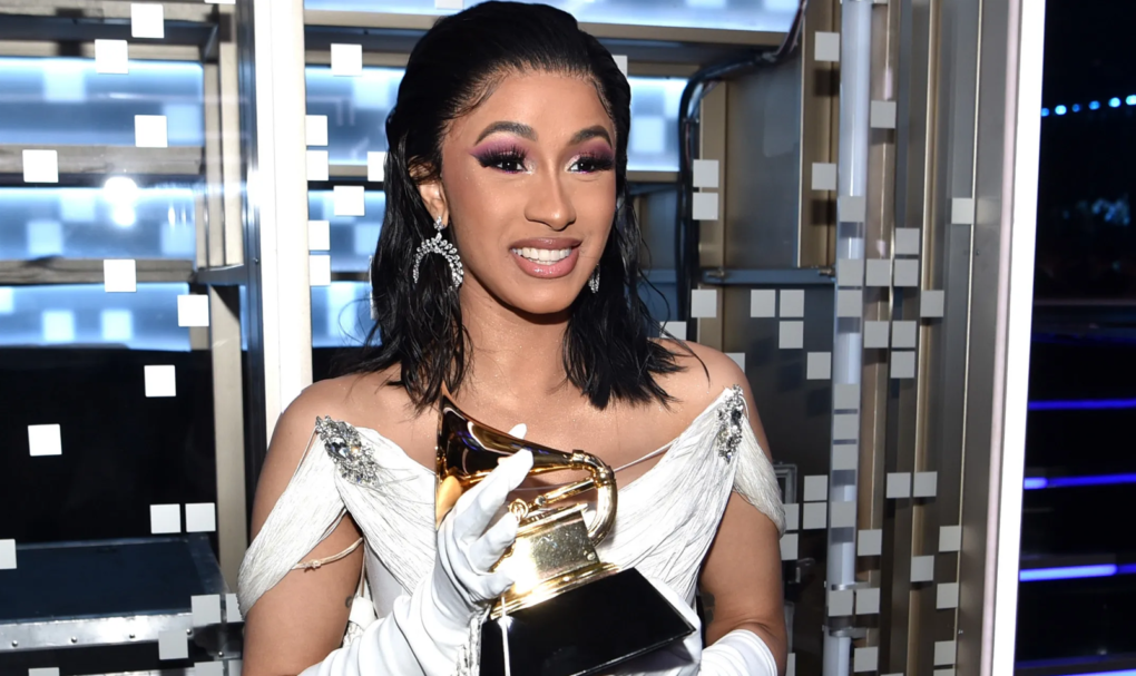 Cardi B holds a Grammy statuette in a white dress and gloves