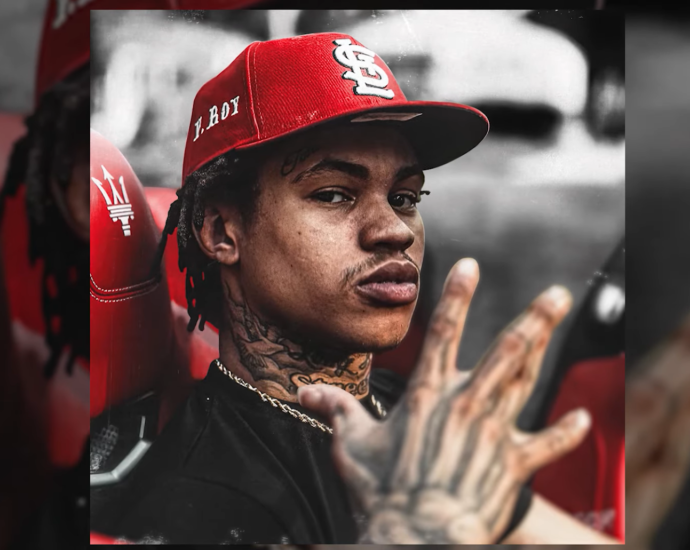 30 Deep Grimeyy in red hat looking at the camera with a raised hand up