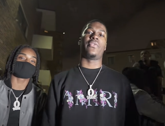 muwop in black t-shirt with silver chain near other man standing near building