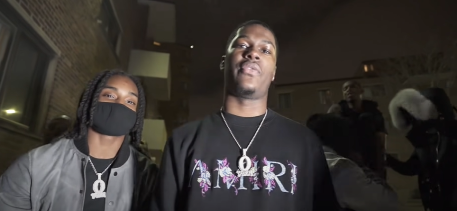 muwop in black t-shirt with silver chain near other man standing near building
