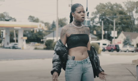 Photo of a woman wearing a tube top, with visible tattoos, standing outdoors and singing