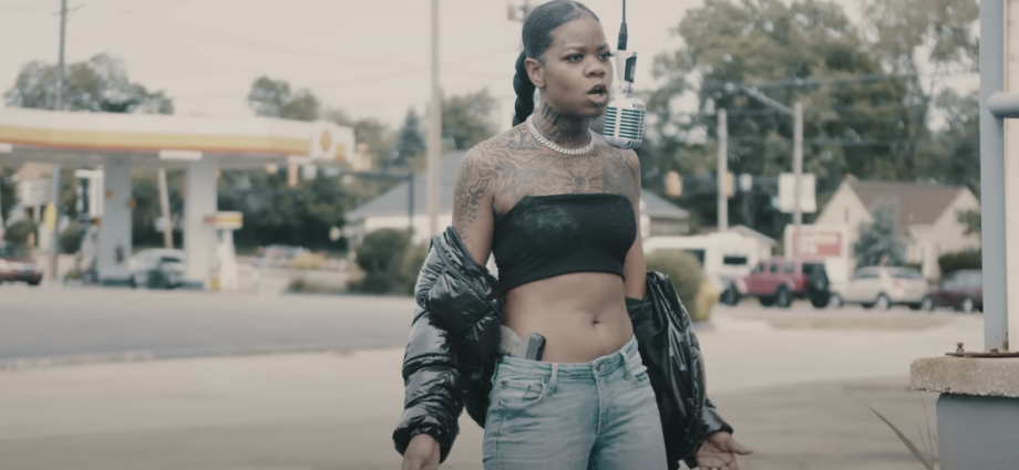Photo of a woman wearing a tube top, with visible tattoos, standing outdoors and singing