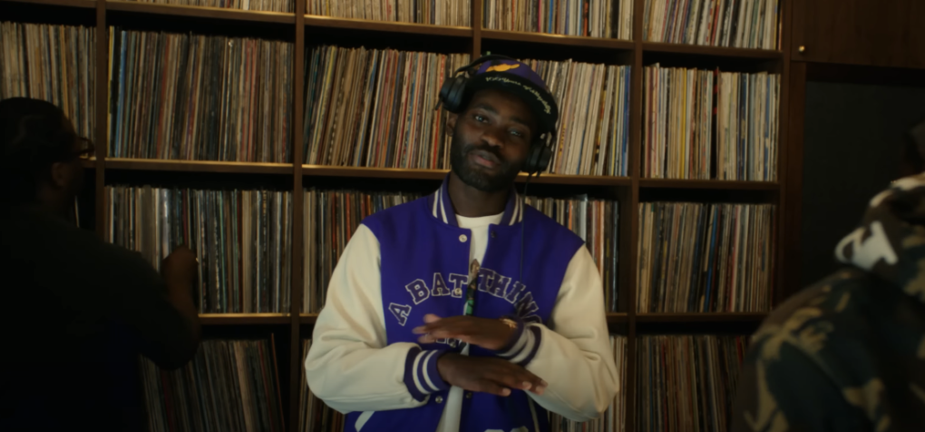 Photo of a man wearing a varsity jacket and a headset, making hand gestures