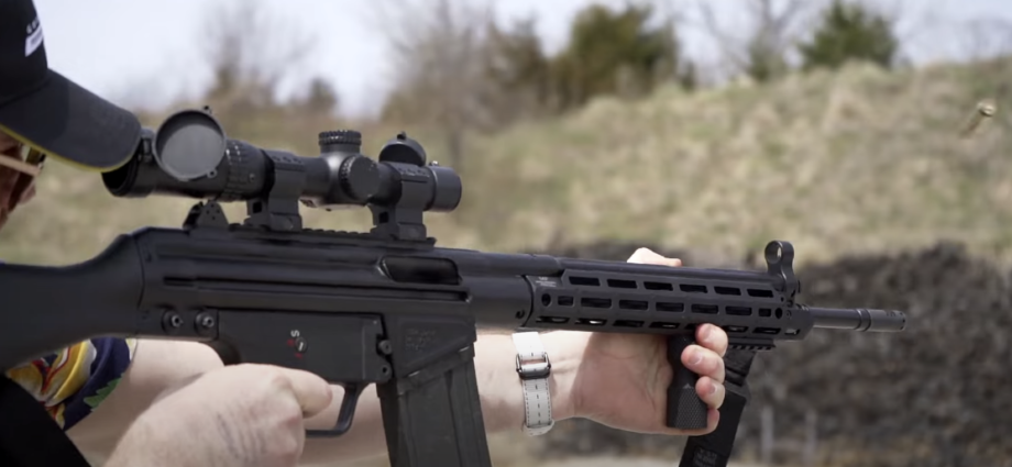 Photo of a guy wearing a hat, holding an automatic firearm