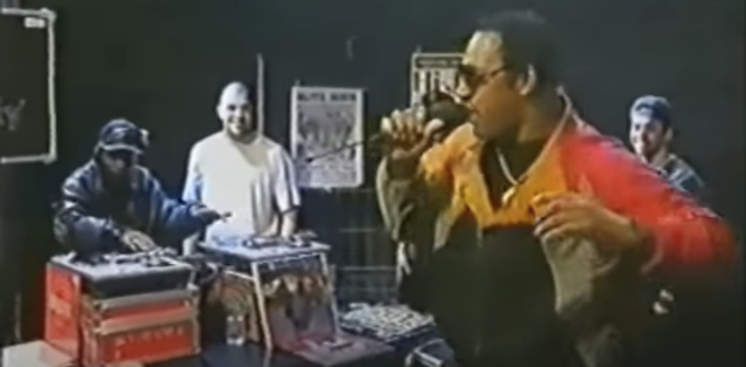 Photo of DJ Kool Herc holding a microphone while singing