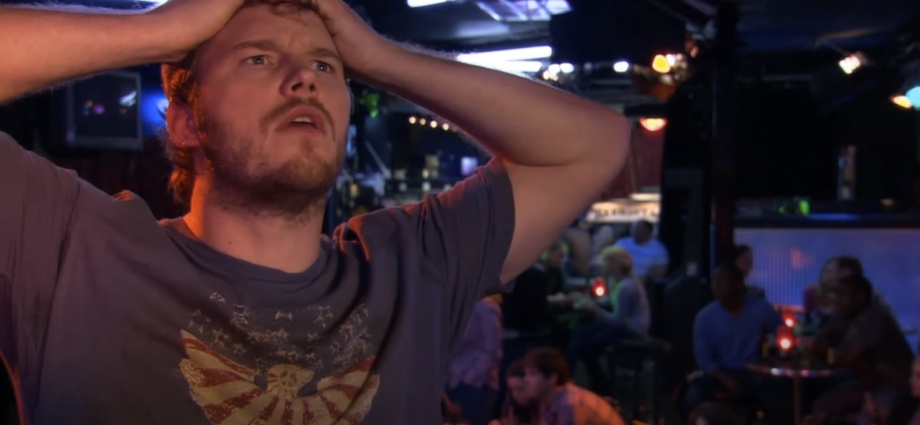 Photo of a man inside a bar, holding his head with both hands, appearing deep in thought